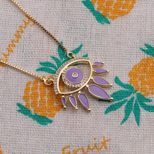 Close-up of golden evil eye necklace with purple enamel and white crystals on fabric