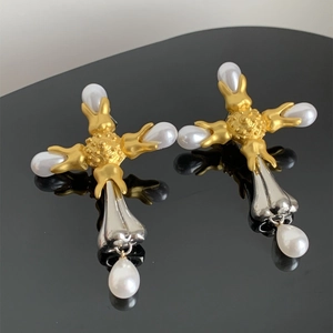Close-up of vintage cross earrings with mixed gold-silver finish and pearl drop charms