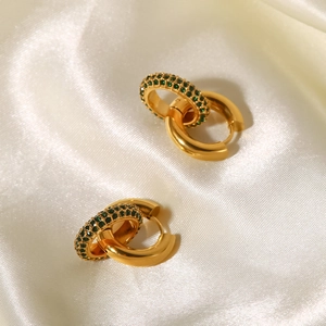 Detailed close-up of gold-plated earrings with green zircon on white silk background