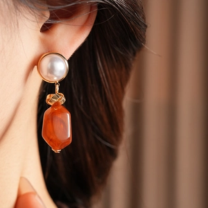 Close-up of irregular orange resin earring with a white pearl and golden metal ring