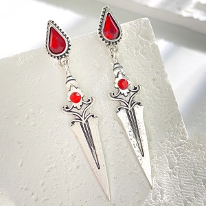 Macro detail of gothic silver sword earrings with red gemstones on white stone base