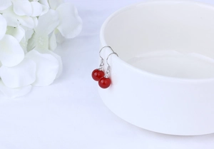 Detail of red agate bead earrings with silver hooks hanging on white ceramic bowl