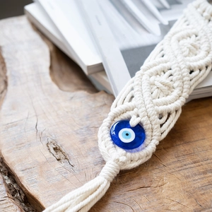 Detail of macrame evil eye wall hanging with white cotton ropes and blue glass bead