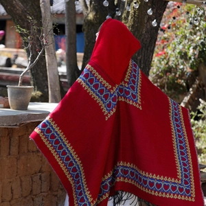 Détail d'une cape rouge ethnique à capuche avec bordure cœur bleu et des franges
