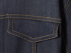 Détail macro d'une poche de veste en jean bleu foncé avec coutures orange contrastées