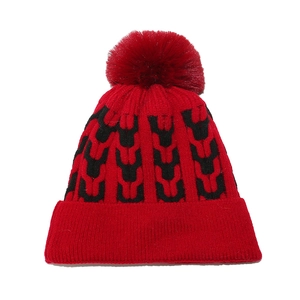 Close-up of red knitted winter hat featuring black jacquard patterns and a faux fur pom-pom