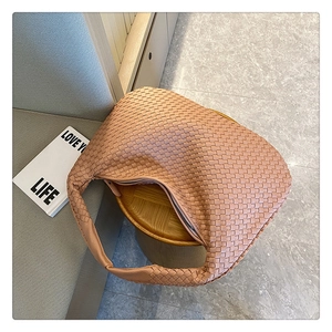 Detailed close-up of a light brown woven hobo bag displayed on a stylish wooden stool