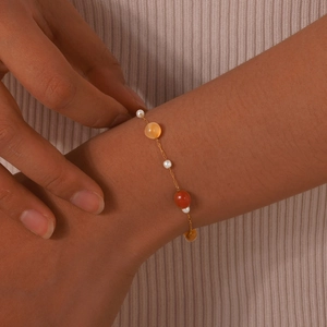 Detail of gold-plated chain bracelet with white pearls and amber-style beads on wrist