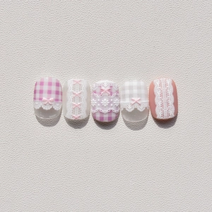 Detailed view of pink gingham nail art with white lace patterns and 3D bow accents
