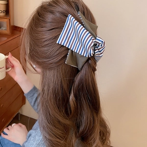Détail d'une pince à cheveux avec nœud rayé portée par un mannequin dans un cadre doux