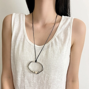 Detail of silver irregular oval pendant on black cord worn by a model for a stylish look