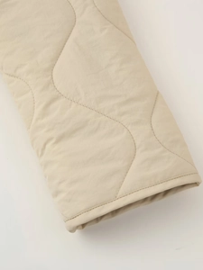 Macro view of beige quilted jacket sleeve with wavy texture and fine stitching detail