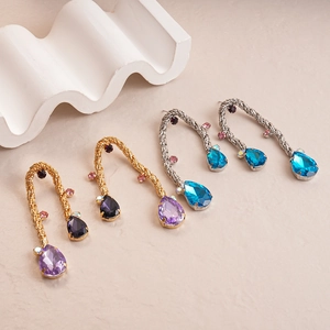 Vintage woven metal teardrop earrings with purple and blue crystals on textured surface