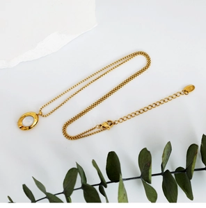 Detail of gold oval shell necklace with 18K hallmark on chain near green leaves