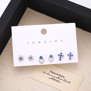 Detalle del juego de pendientes de flores y cruces de cristal azul en tono plateado