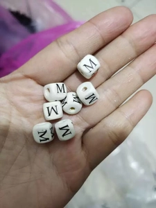 Detail shot of white square acrylic beads with black letter M for DIY jewelry making