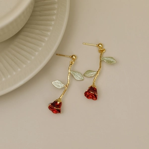 Elegant red rose earrings with golden stem and green leaves on a ceramic plate
