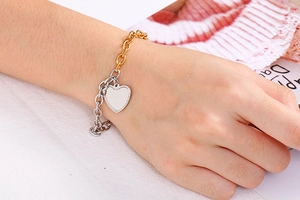 Detail of two-tone gold and silver chain bracelet with heart charm on a model's wrist