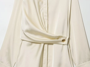 Détail de chemisier satiné crème avec torsion à la taille et bouton doré élégant en gros plan