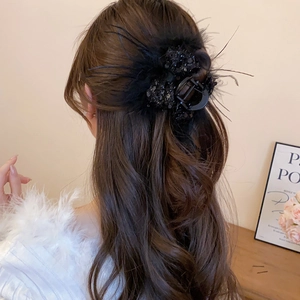 Detail of a large feather and sequin bow hair claw clip styled on long wavy hair