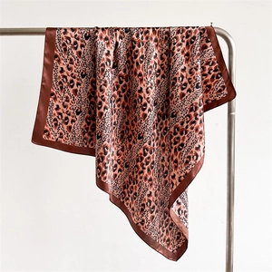 Detailed view of leopard print satin silk scarf with brown hem on a metal hanger