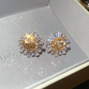 Macro detail of champagne cushion-cut zircon earrings with baguette petals in a box