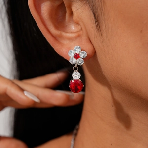 Close-up of floral drop earrings featuring red zircon gemstones and silver metal finish