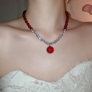 Detail of red beaded necklace with large spherical pendant on elegant female model