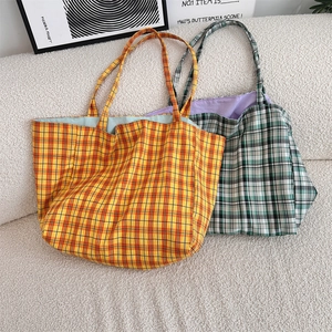 Close-up of reversible checkered canvas tote bags in orange and green on a soft beige sofa