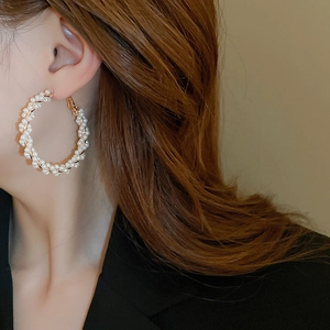 Gros plan d'une femme portant de grandes boucles d'oreilles créoles en perles et fil doré