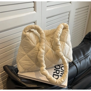Detailed view of cream-colored quilted down shoulder bag on a leather sofa
