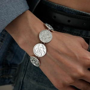 Detail of silver link bracelet with vintage relief coins on a model wearing denim