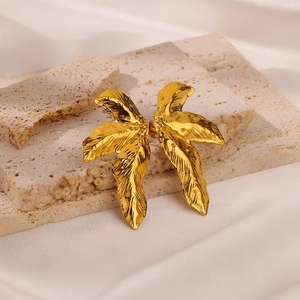 Macro detail of gold leaf earrings with intricate wing-like textures on a stone surface