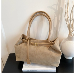 Detail of a large khaki suede tote bag with long handles placed on white books