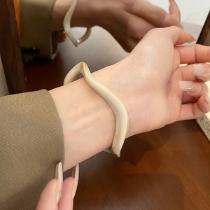 Detail of cream wavy resin bangle with smooth texture worn by a model in soft lighting