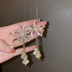 Gros plan de longues boucles d'oreilles fleurs avec zircons roses et franges dorées