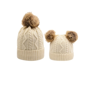 Flat lay of cable knit parent-child hat set with faux fur pom-poms in off-white
