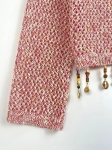 Detail of pink knit top featuring hollow-out mesh texture with shell and tassel fringe