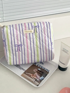 Quilted makeup bag with purple stripes and bow pattern on a white marble countertop