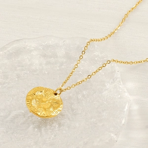 Detail of gold starburst necklace with radial textured pendant on glass plate