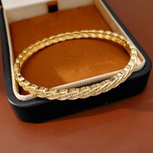 Close-up of gold-plated twisted bangle with shimmering cubic zirconia in premium gift box