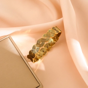 Detailed view of 18K gold plated layered wave bangle on a soft pink silk background