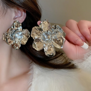 Macro detail of large metallic silver flower earrings with artistic pleated texture