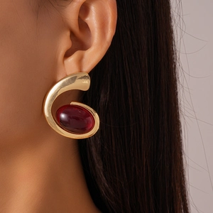 Close-up of gold irregular geometric earring with a large deep red oval resin stone
