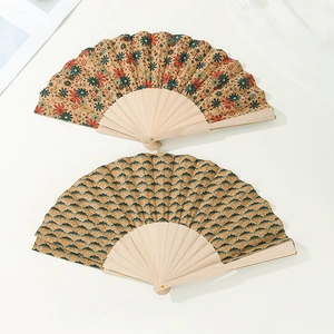 Detail view of two vintage cork folding fans with floral and wave patterns on light wood