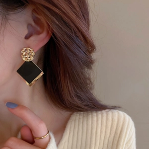 Close-up of geometric gold-textured stud and black diamond pendant earring on model