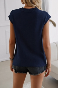 Back view of a sleeveless navy blue knit sweater vest top on a model in a minimal interior