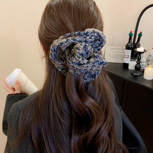Détail d'un chouchou en tricot à carreaux bleus porté par un mannequin dans un café chic