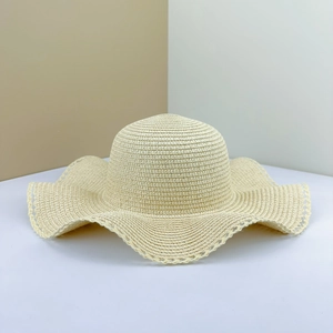 Close-up of beige straw sun hat featuring wavy brim and elegant hollow lace trim detail
