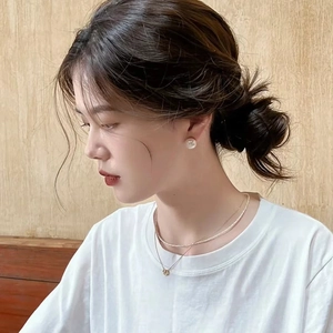 Close-up of natural pearl stud earrings and a layered gold necklace on a model